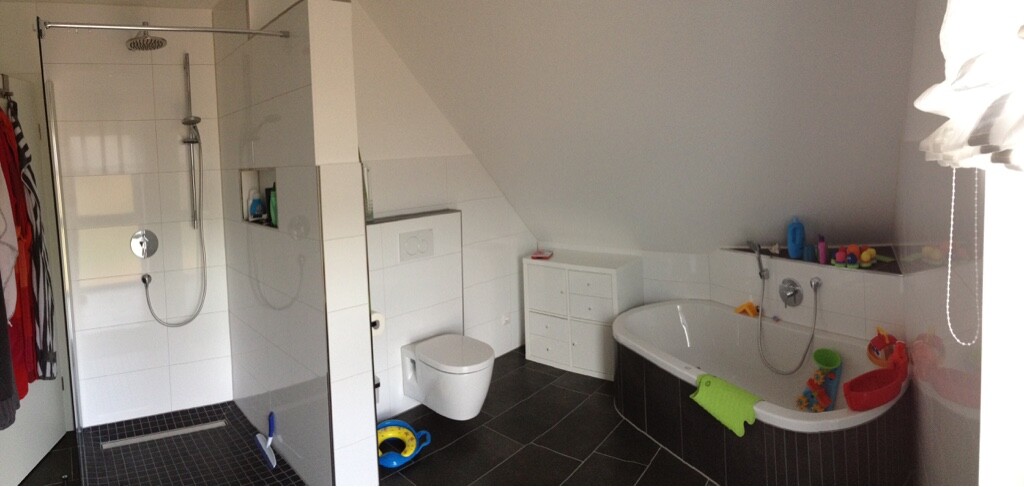Helles Badezimmer mit Dusche, Toilette und Eckbadewanne mit Spielzeug.