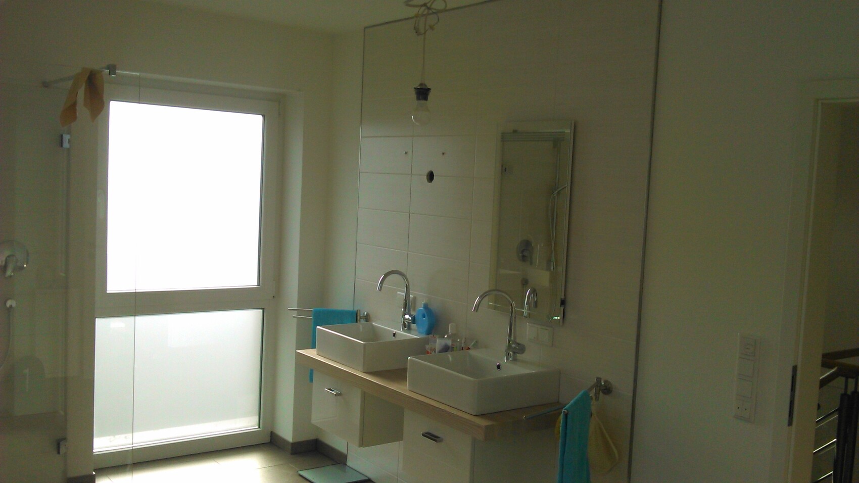 Badezimmer mit Doppel-Waschtisch, zwei Becken, großer Spiegel, Fenster links, blaue Handtücher