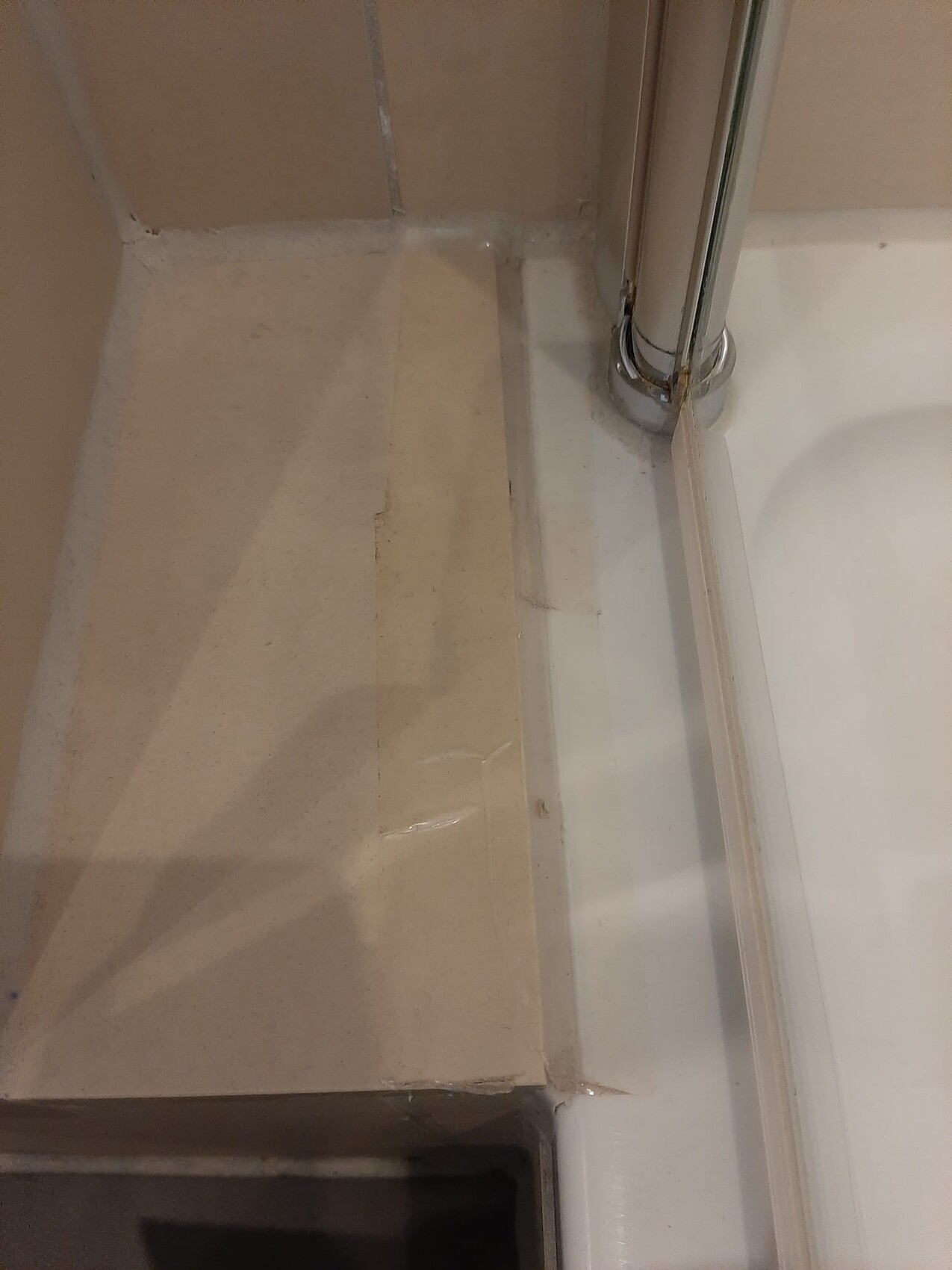 Blick in Dusche: beige Wandfliesen, weisser Boden, verchromte Stange, Silikonfuge an der Ecke.