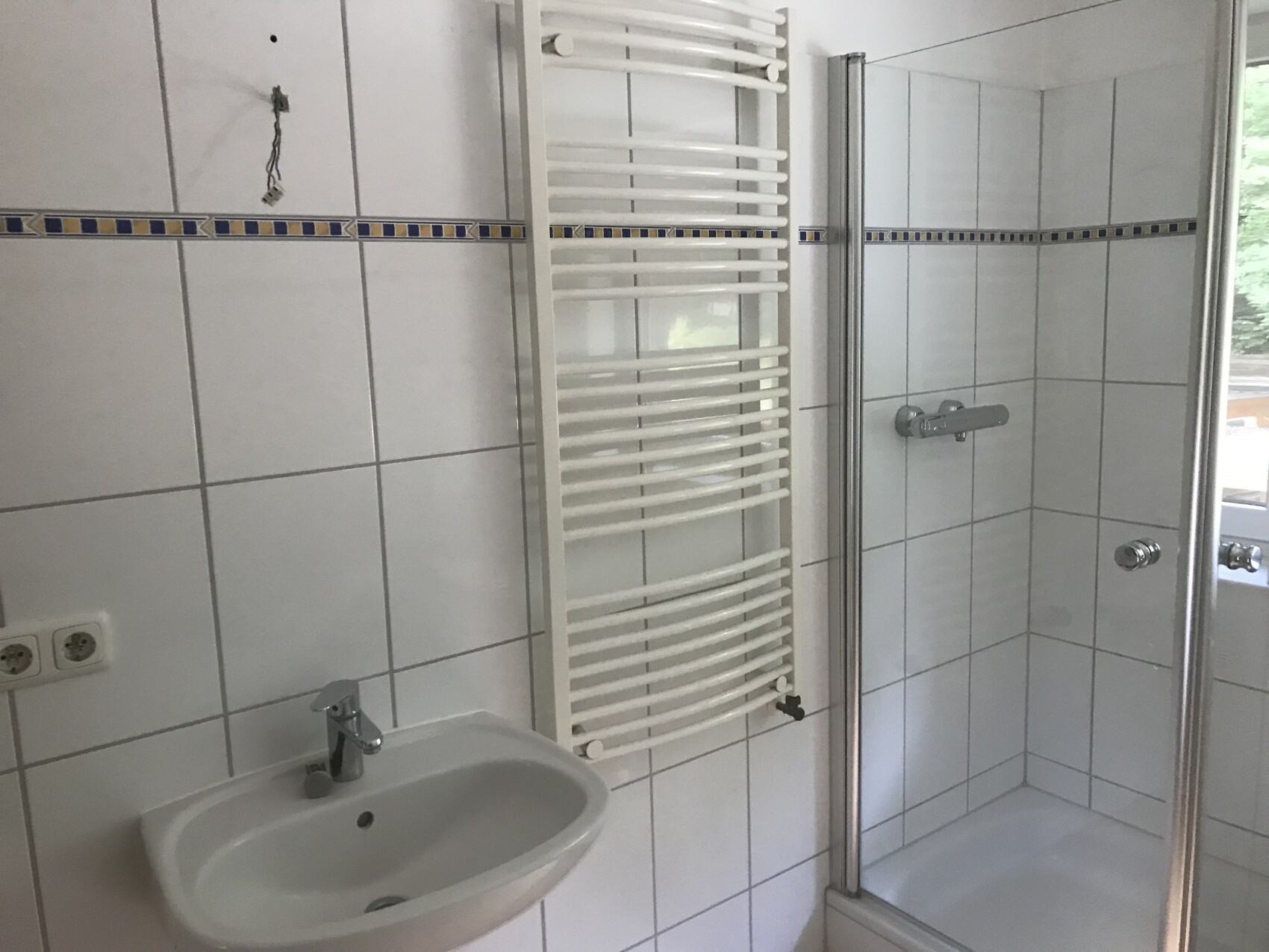 Badezimmer mit Waschbecken, Handtuchheizkörper und Duschkabine; weiße Fliesen mit blauer Bordüre