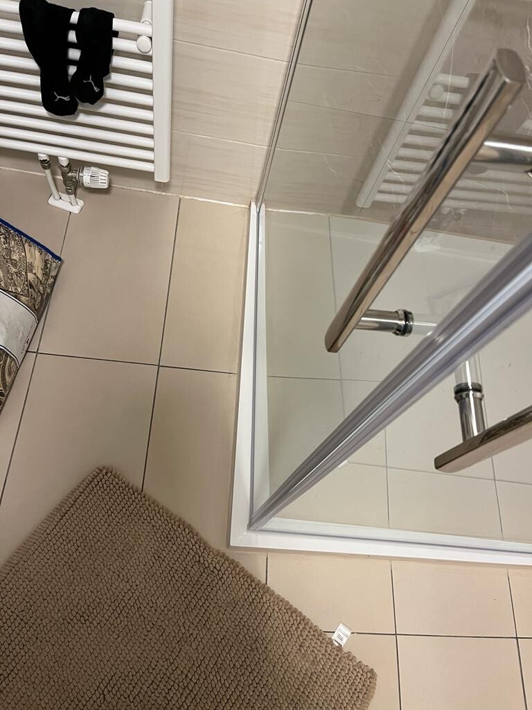 Badezimmer mit Glasdusche, Handtuchheizkörper, schwarze Socken und beige Fliesen.