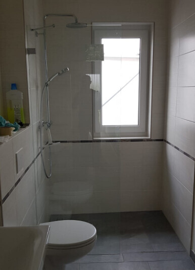 Badezimmer mit Glasdusche, Toilette und Fenster
