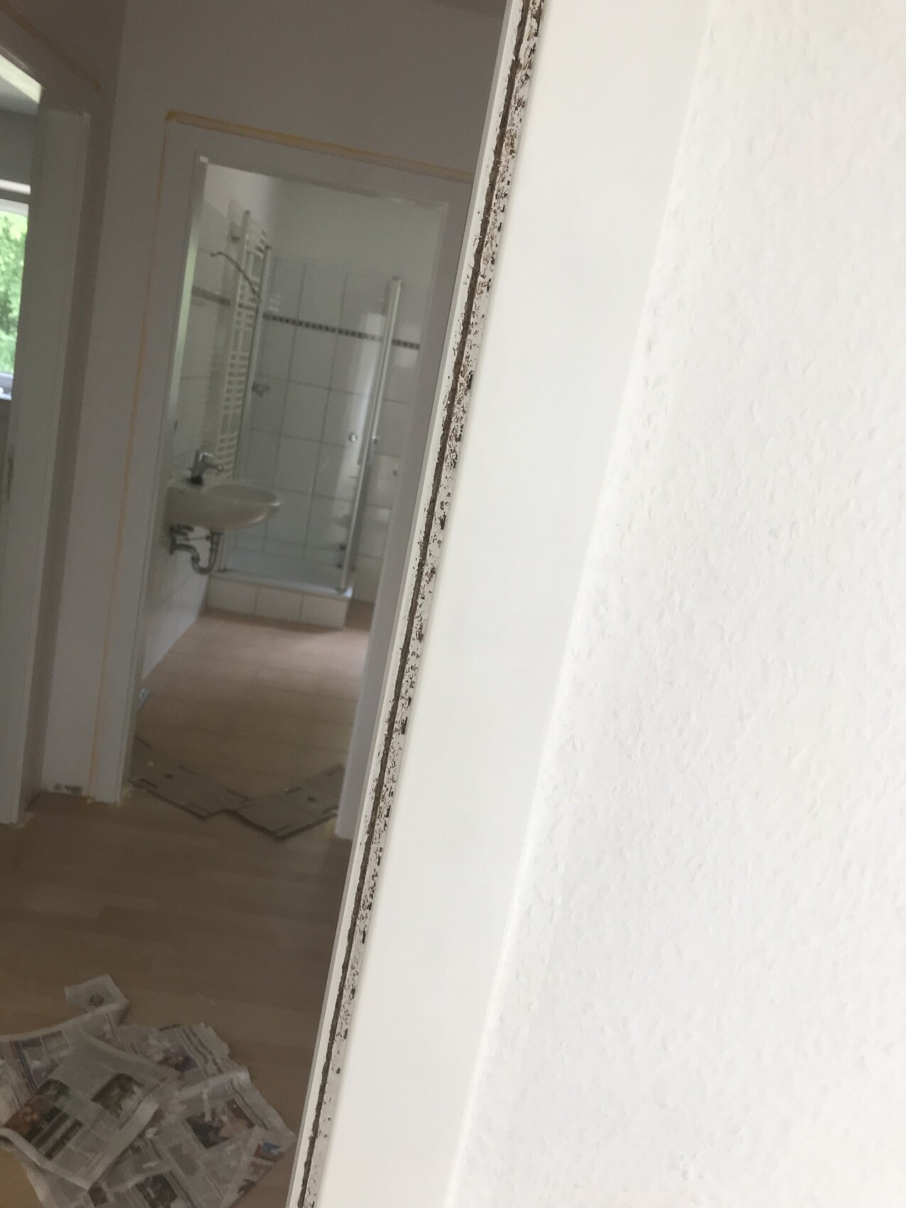 Badezimmer mit Waschbecken, Dusche, Fliesenwand und Zeitungen auf dem Boden