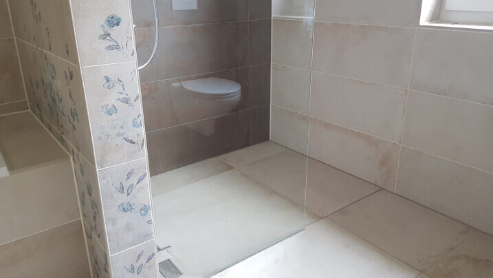 Badezimmer mit beigen Fliesen, Glasdusche und wandhängendem WC.