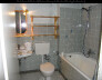 Helles Badezimmer mit Glasdusche, Toilette, Waschbecken und Holzregal