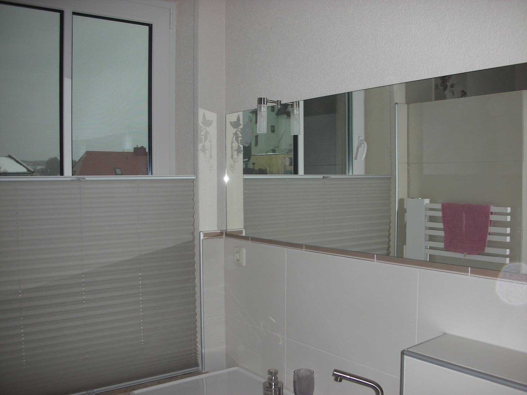 Badezimmer mit Fenster, Jalousie, großem Spiegel, Waschbecken und rosa Handtuch.