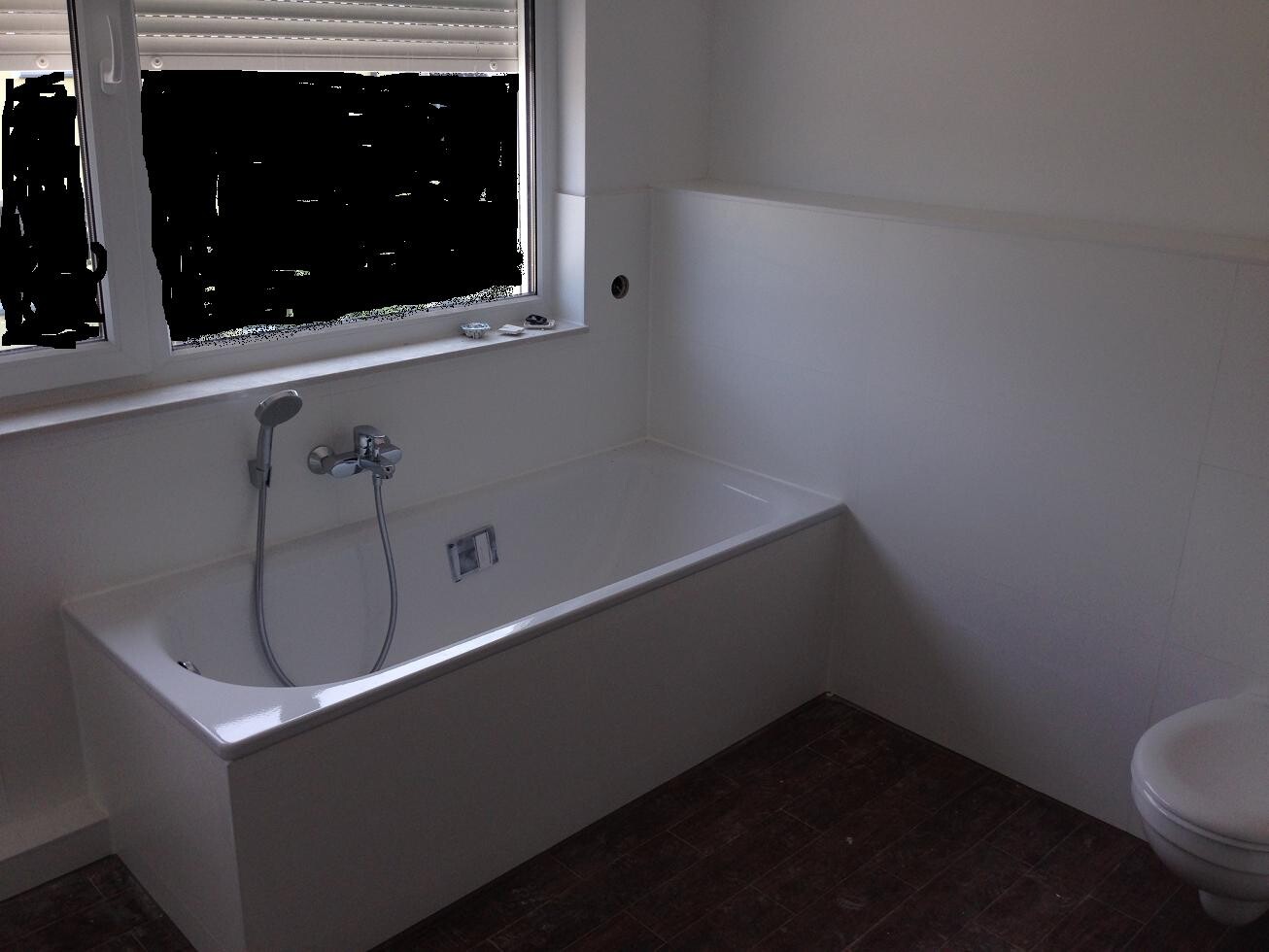 Helles Badezimmer mit weißer Badewanne, Fenster und Toilette, weiße Fliesen.