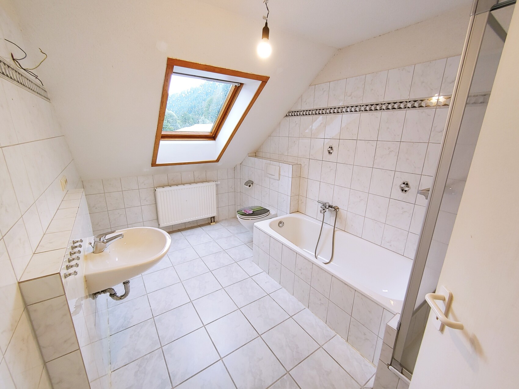 Helles Badezimmer mit Dachfenster, Badewanne, Waschbecken, Toilette und Fliesen.