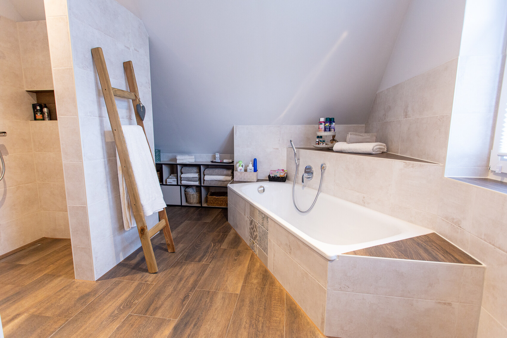 Modernes Badezimmer mit Eckbadewanne, Holzfußboden, Leiter mit Handtuch und Regal mit Handtüchern.