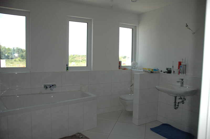 Helles Bad mit Badewanne links, Toilette in Mitte, Waschbecken rechts; Fenster hinten.