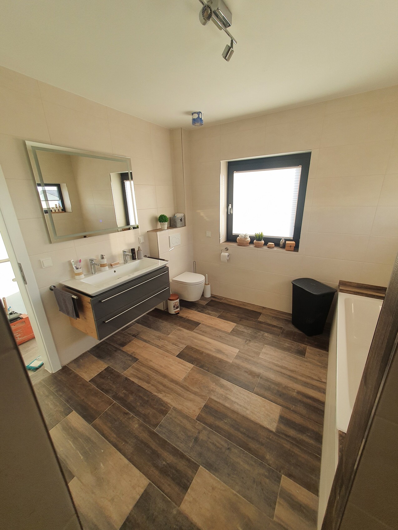 Modernes Badezimmer mit Waschtisch, Spiegel, Toilette, Badewanne und Fenster.