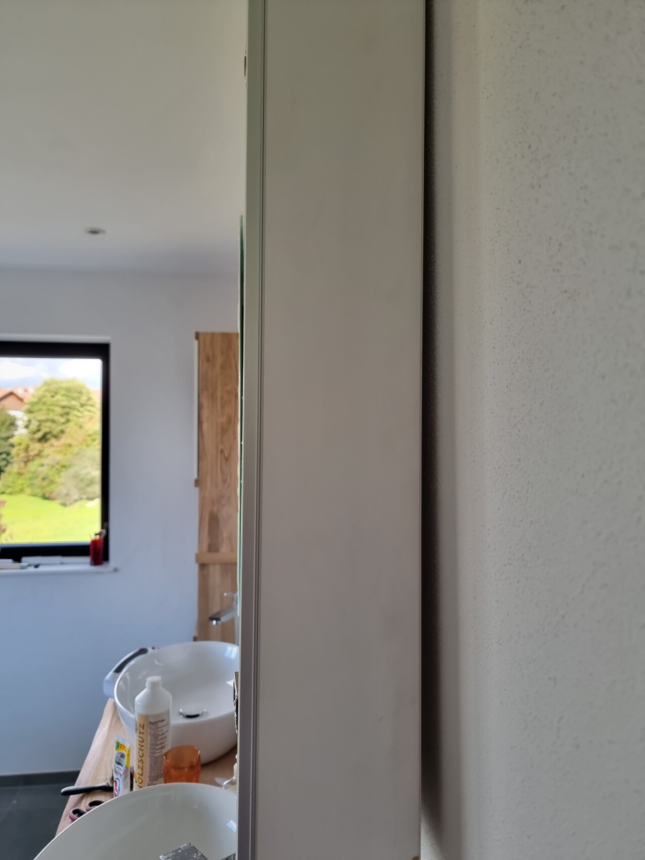 Küchenbereich mit Waschbecken auf Holzplatte, Reinigungsmittel und Fenster mit Gartenblick.