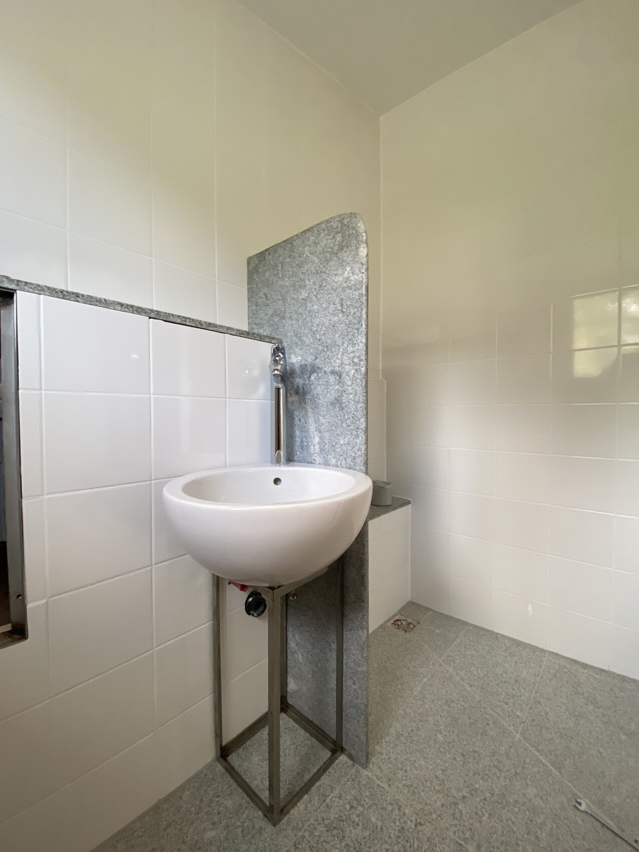 Weiße runde Waschschüssel auf Metallgestell vor grauer Granitwand im Badezimmer.