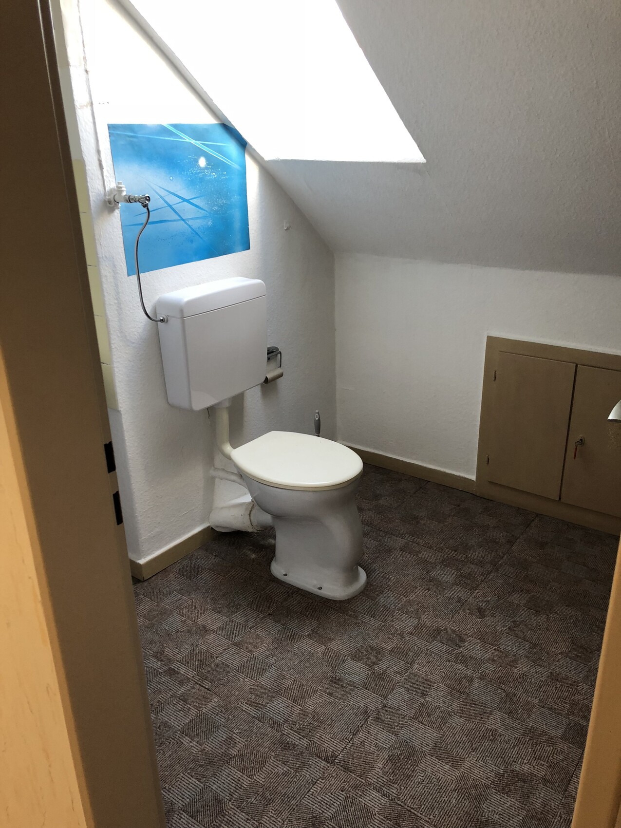 Kleines Badezimmer im Dachgeschoss mit Toilette, Spülkasten, Dachfenster und Unterschrank.