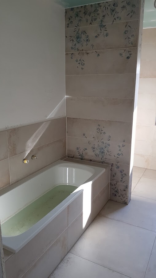 Badezimmer mit weißer Badewanne, grünem Wasser und Wandfliesen mit Blumenmuster.
