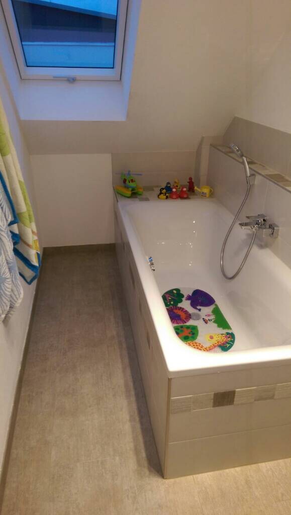 Badezimmer mit Badewanne unter Dachfenster; bunte Spielzeugfiguren am Wannenrand.