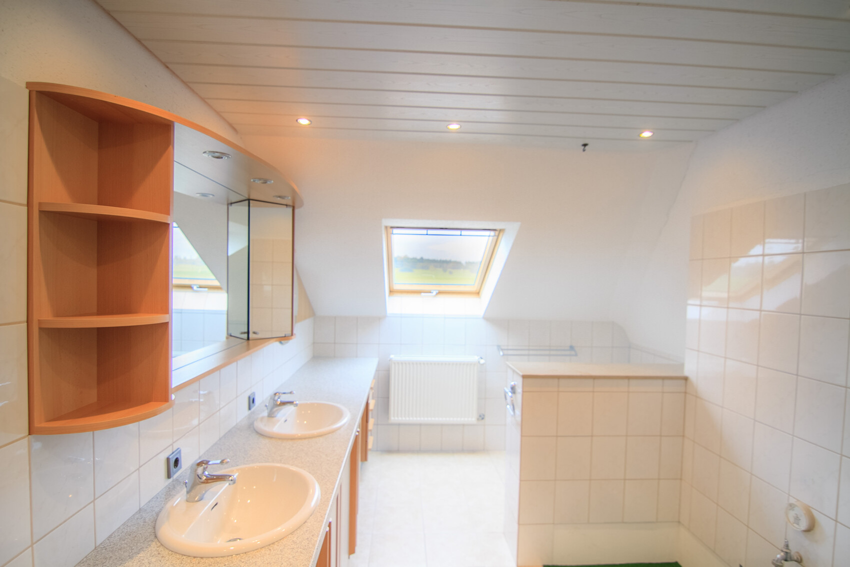 Helles Badezimmer mit zwei Waschbecken, Spiegeln, Holzregal und Dachfenster im Dachraum.