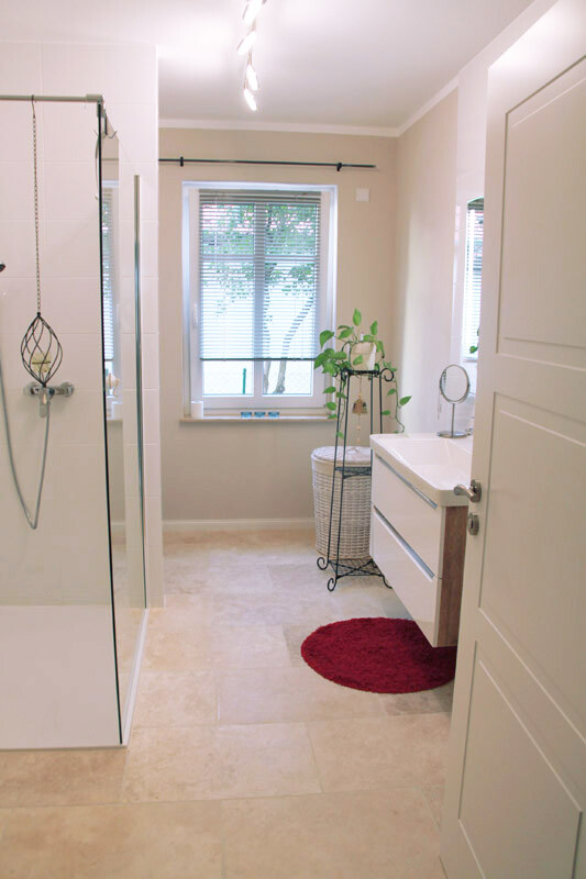 Modernes Badezimmer mit Dusche, Fenster, Waschtisch, Pflanze und rotem Teppich.