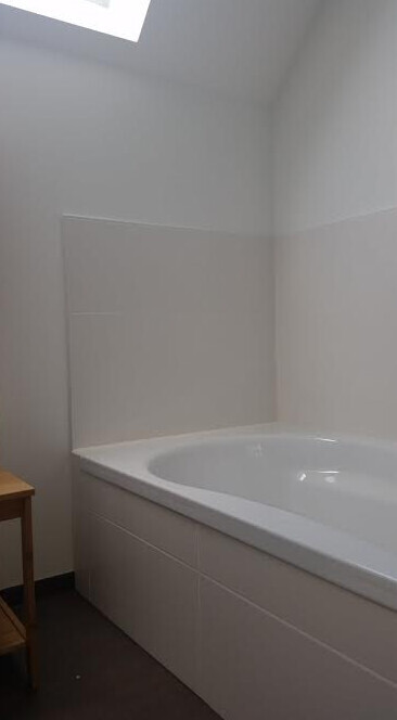 Weißes Badezimmer mit eingebauter Badewanne, weißen Fliesen und Dachfenster.