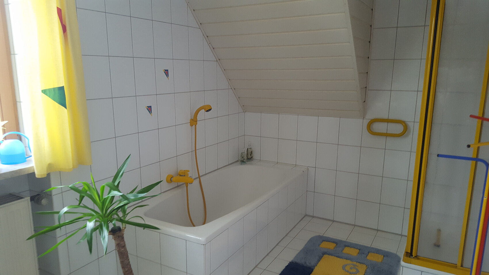 Helles Badezimmer mit Badewanne, gelben Armaturen, Dusche und schräger Decke