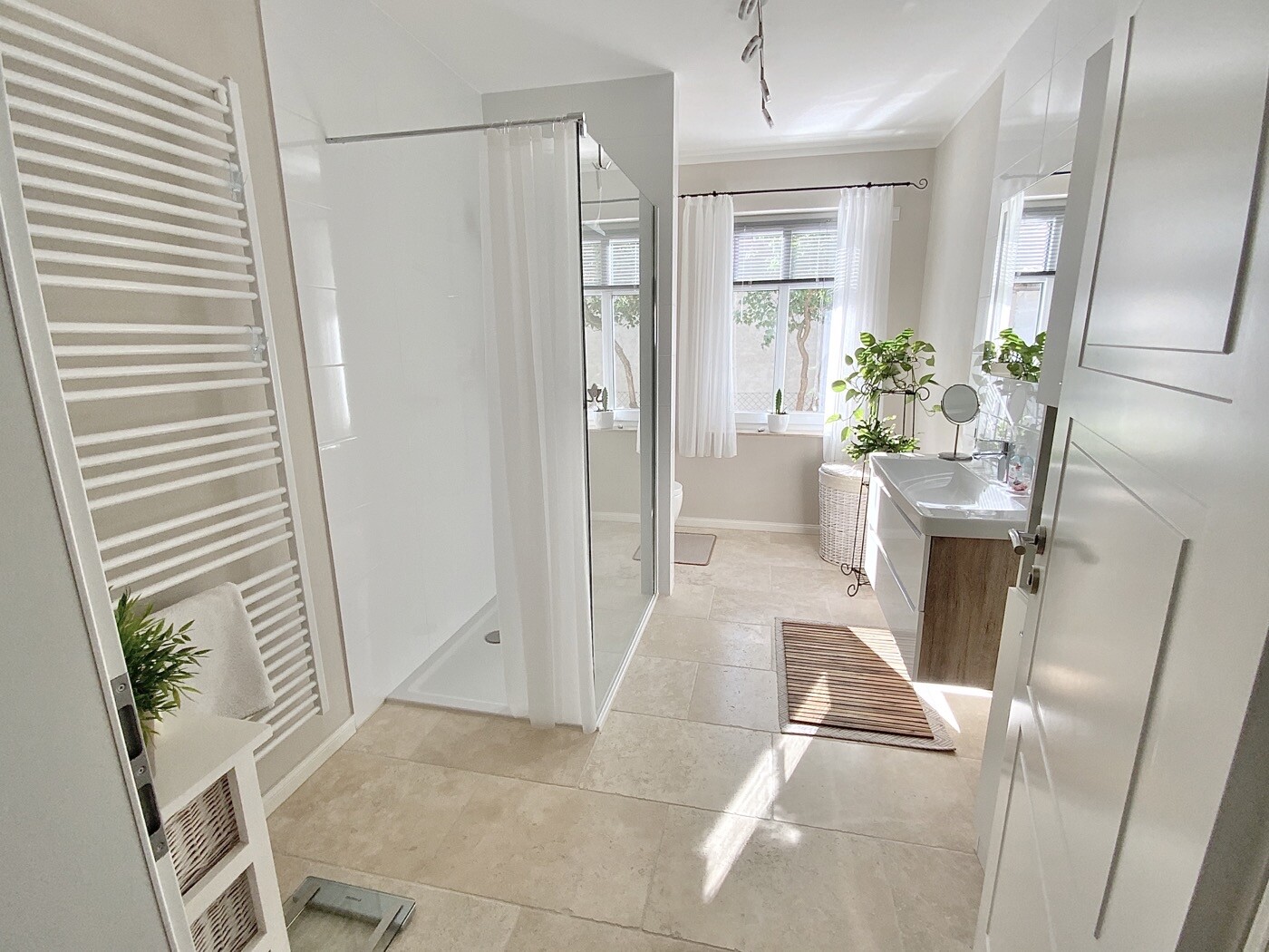 Helles Badezimmer mit Glasduschkabine, Waschbecken, Fensterfronten, Vorhängen und Pflanzen