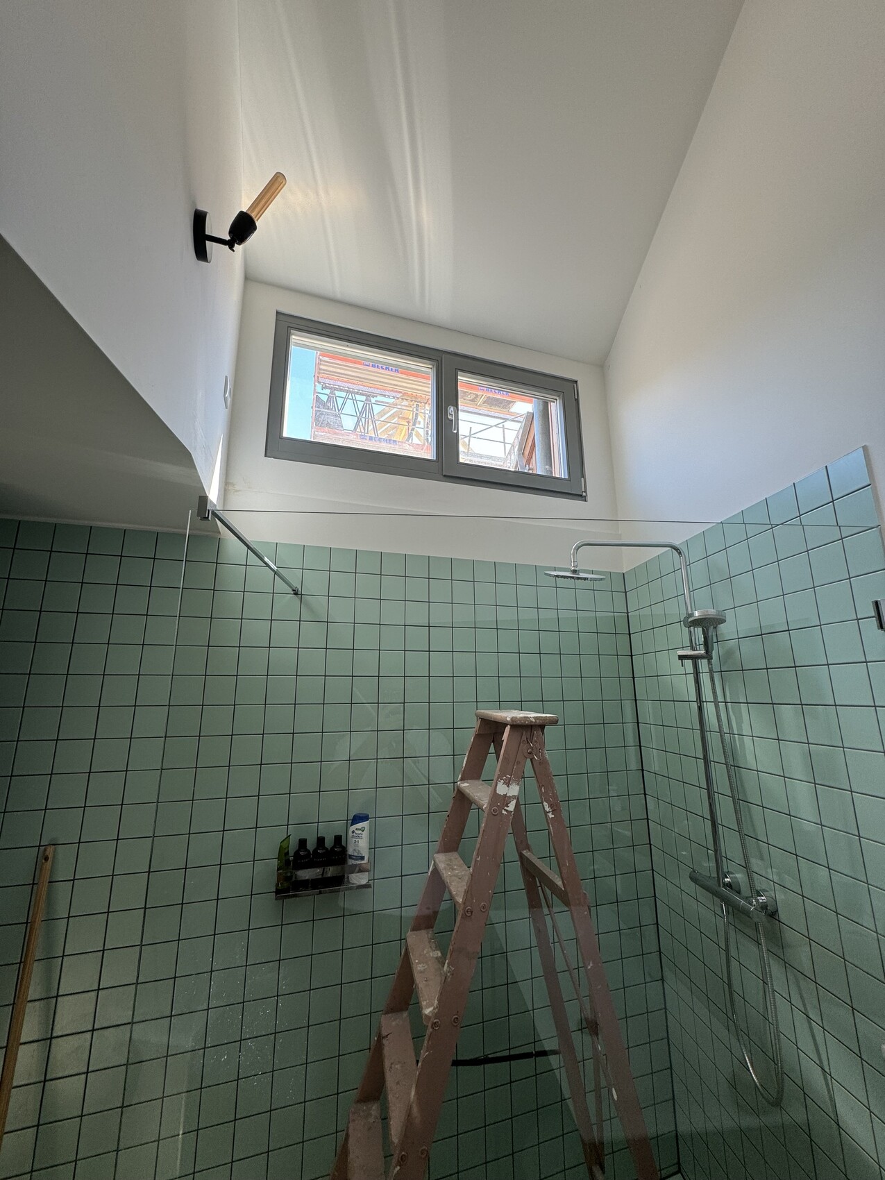Badezimmer unter Renovierung: mintgrüne Fliesen, Leiter, Duschbereich und Fenster hoch oben.