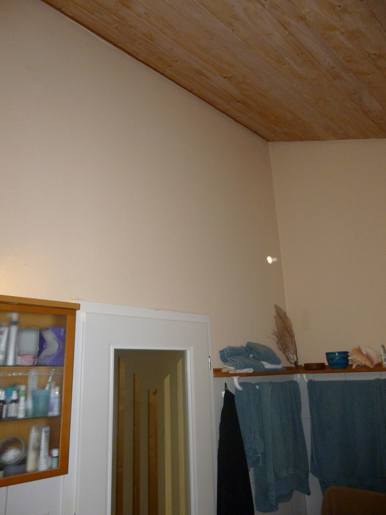 Badezimmer-Ecke mit Holzbalkendecke, Tür, Regal mit Badutensilien, Handtücher.