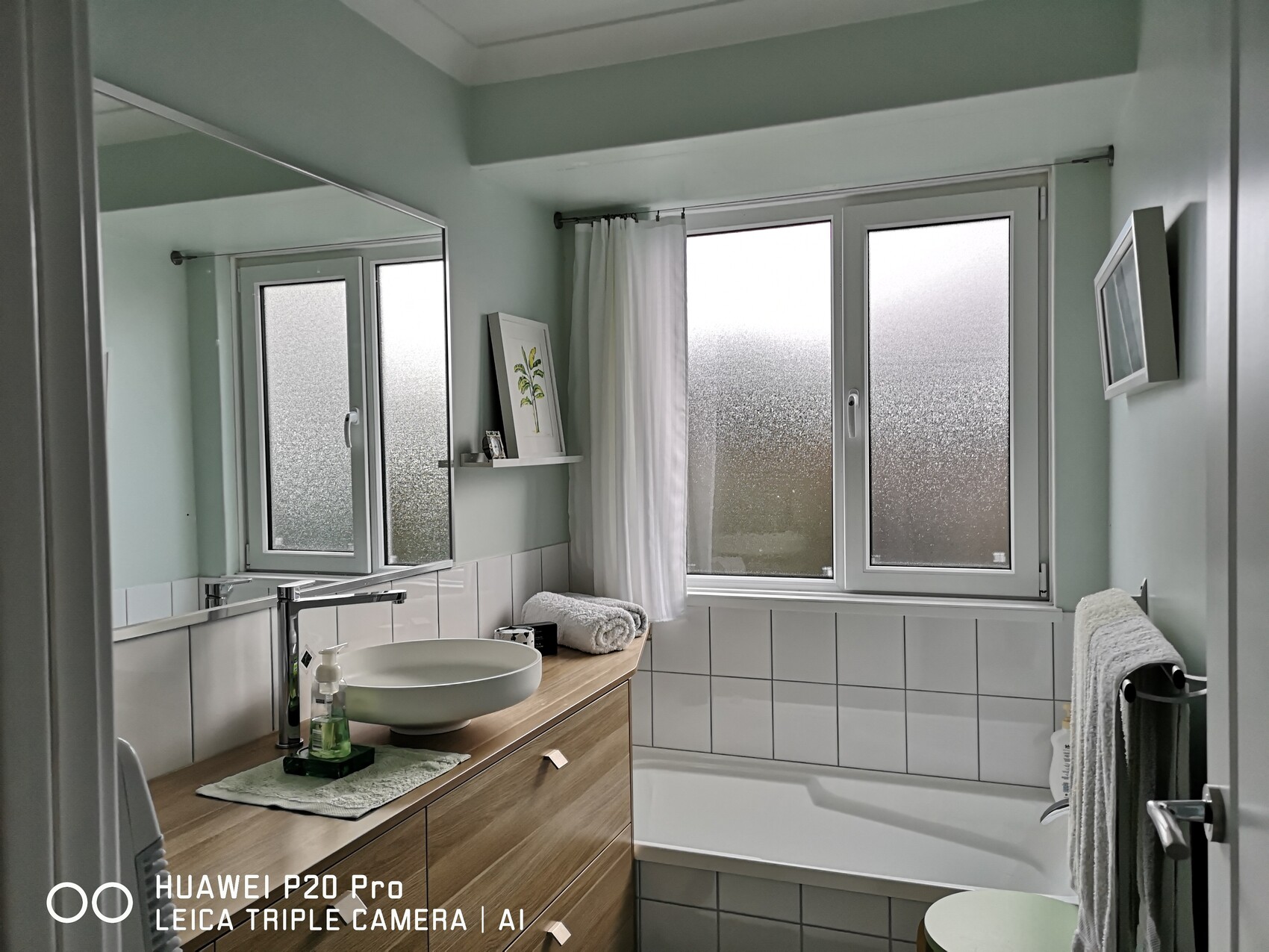 Helles Badezimmer mit mintgrünen Wänden, Waschbecken auf Holzunterschrank, milchigen Fenstern.