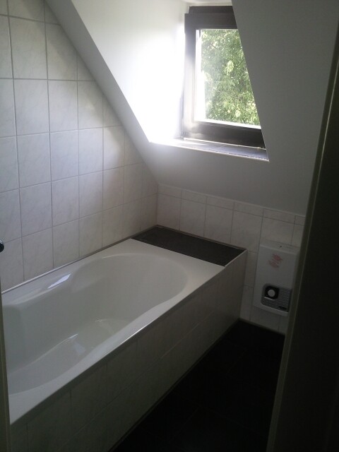 Badezimmer mit weißer Badewanne, Fliesenwänden, Dachfenster und dunklem Boden.