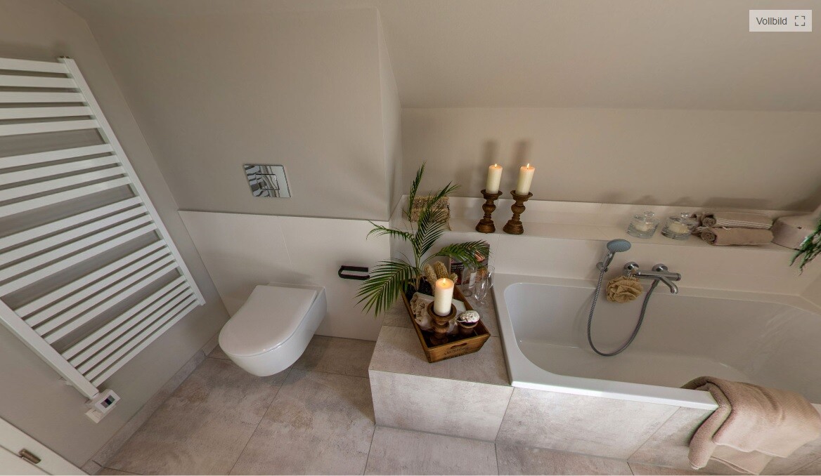 Helles Badezimmer mit Wandtoilette, Badewanne, Deko-Kiste mit Kerzen, Pflanze und Handtüchern.
