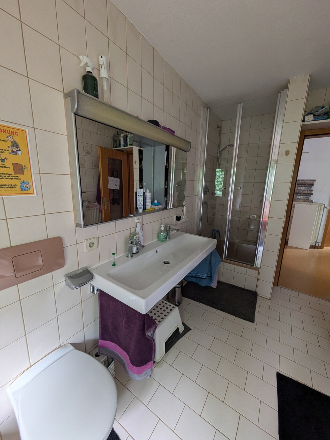 Helles Badezimmer mit Waschbecken, Spiegel, Dusche und Fliesen.