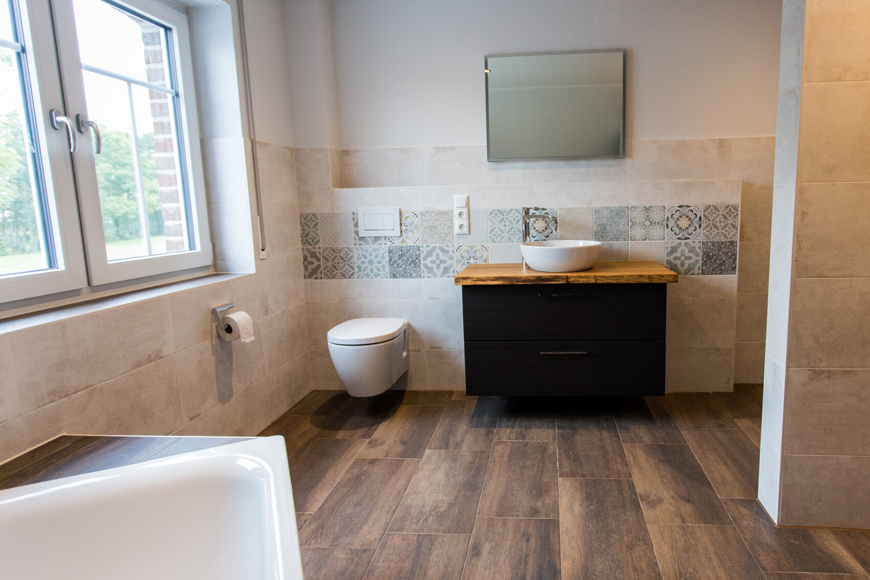 Modernes Badezimmer: Fenster links, wandhängendes WC, Holz-Waschtisch mit runder Spüle, Musterfliesen