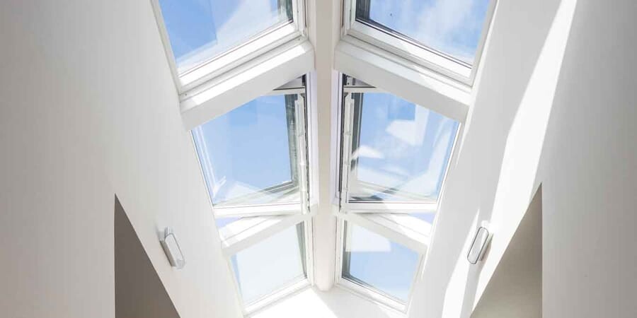 Dachfenster in weißer Zimmerdecke mit Glasfenstern und Blick auf blauen Himmel.