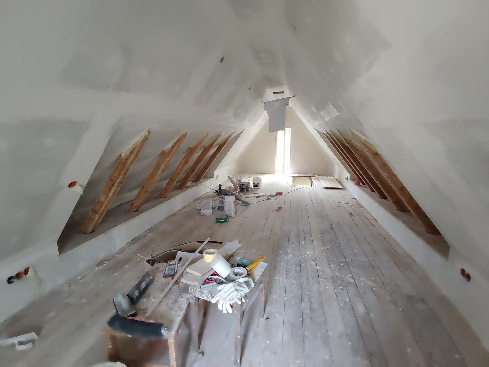 Dachboden im Ausbau: Holzbalken, Werkzeuge und Baumaterialien auf dem Holzboden, Licht am Ende.