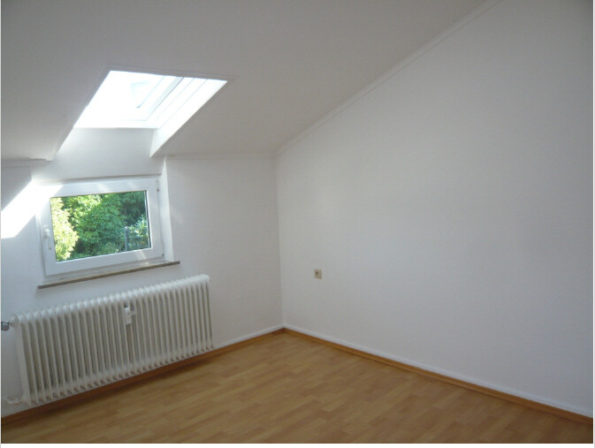 Helles, leeres Dachzimmer mit Holzboden, Heizkörper und Dachfenster; Blick nach Grün.