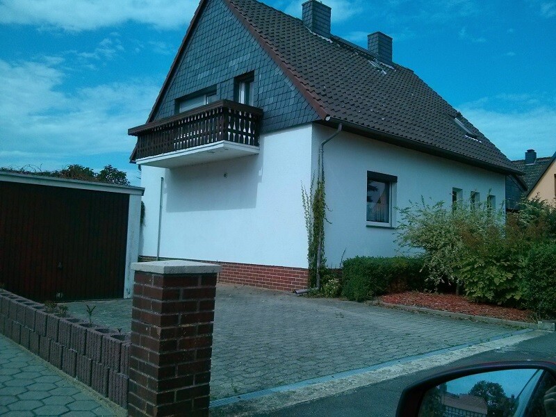 Weißes Einfamilienhaus mit Satteldach, Balkon und gepflasterter Einfahrt.