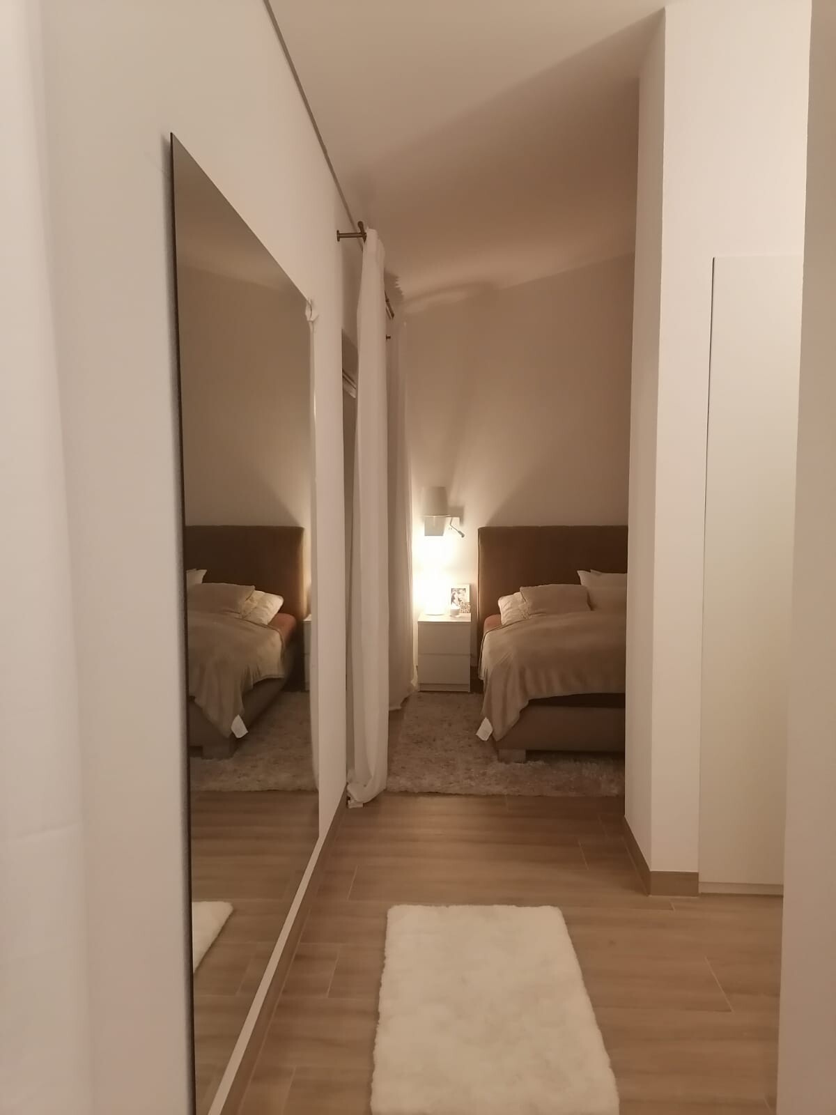 Hotelzimmer mit zwei Betten, Nachttisch und Lampe, Spiegelwand links, Holzboden.
