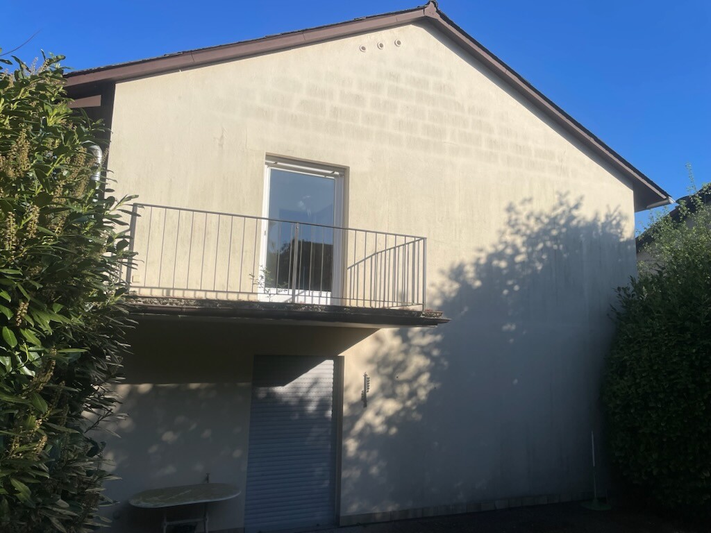 Zweistöckiges Haus mit Balkon, Glas-Tür und Metallgeländer, von Hecken umgeben