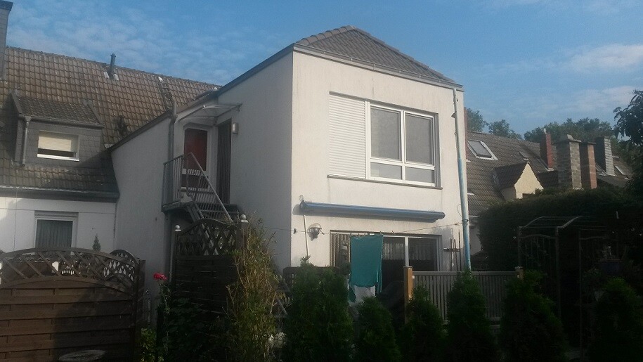 Zweistöckiges, weißes Haus mit Balkon an der linken Seite, Garten und Zaun davor.