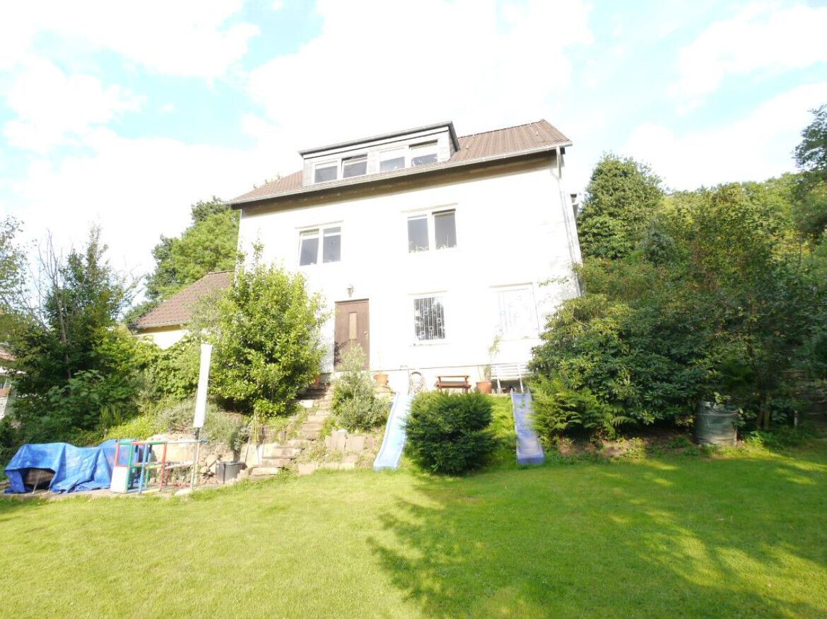 Weißes zweistöckiges Haus mit Garten; zwei Rutschen und Spielgeräte im Vorgarten.