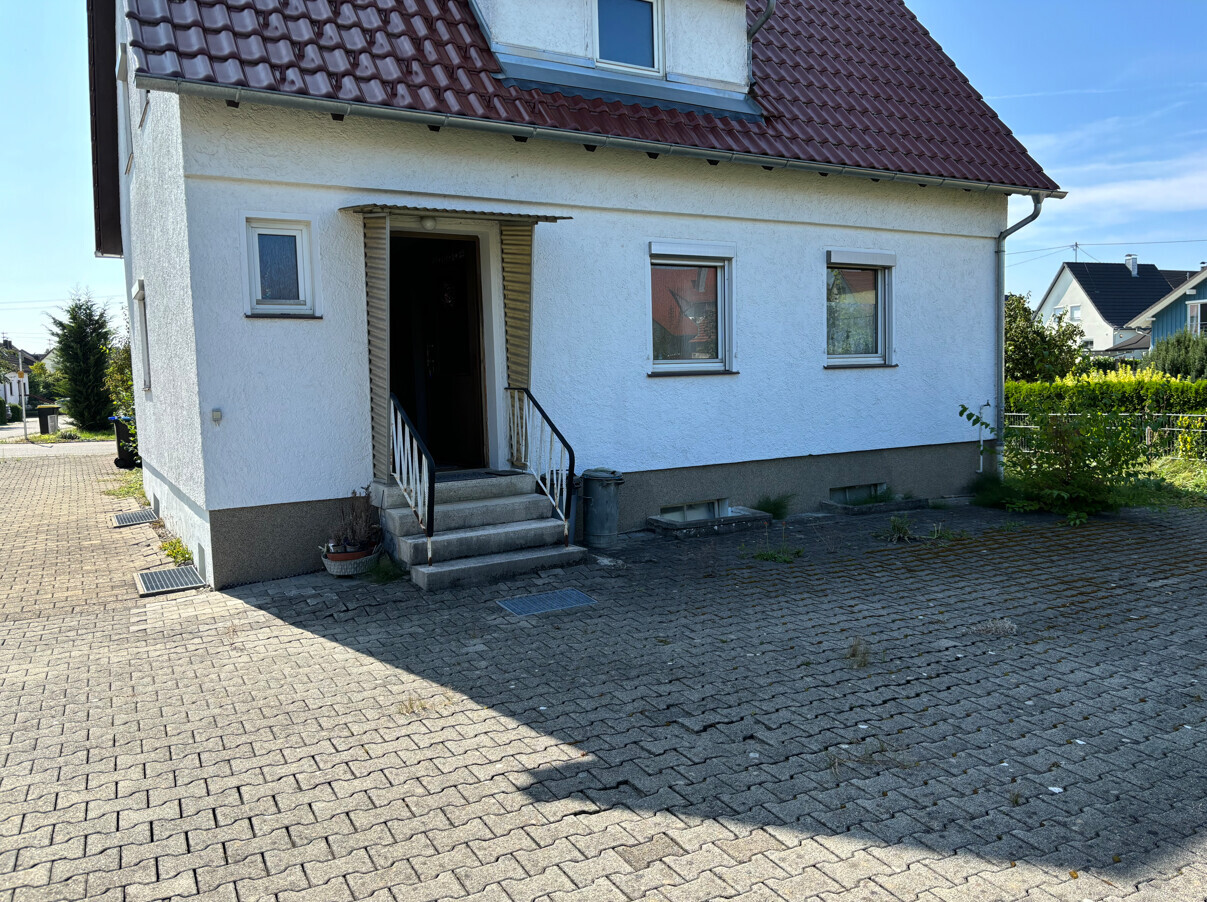 Weiße Hausfassade mit rotem Ziegeldach, offener Eingang, Treppenstufen und gepflasterte Zufahrt