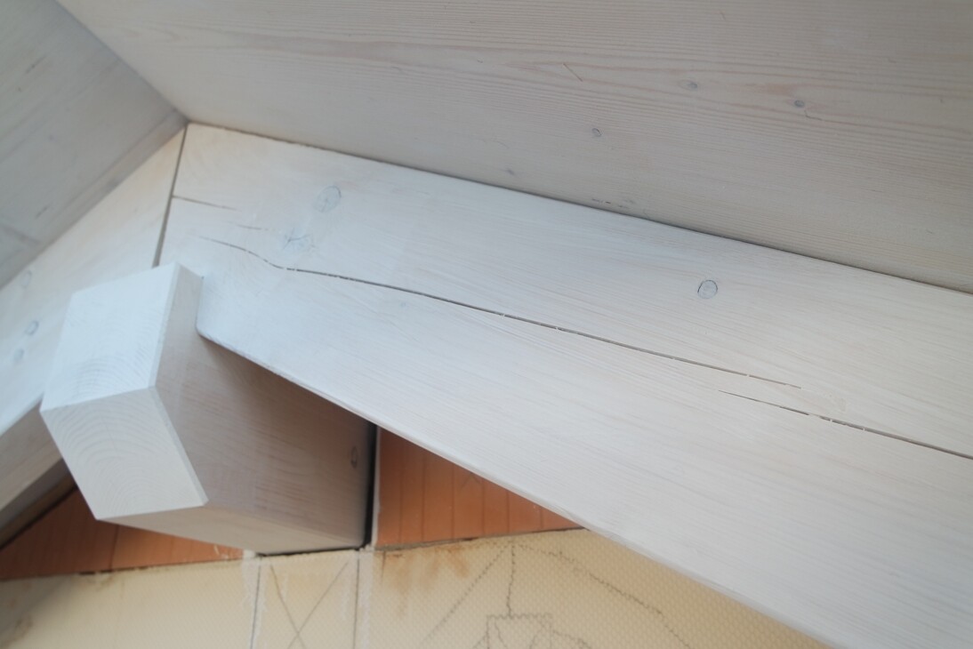 Helle Holzbalken im Dachstuhl; diagonaler Balken trifft auf querliegendes Holzteil mit Block