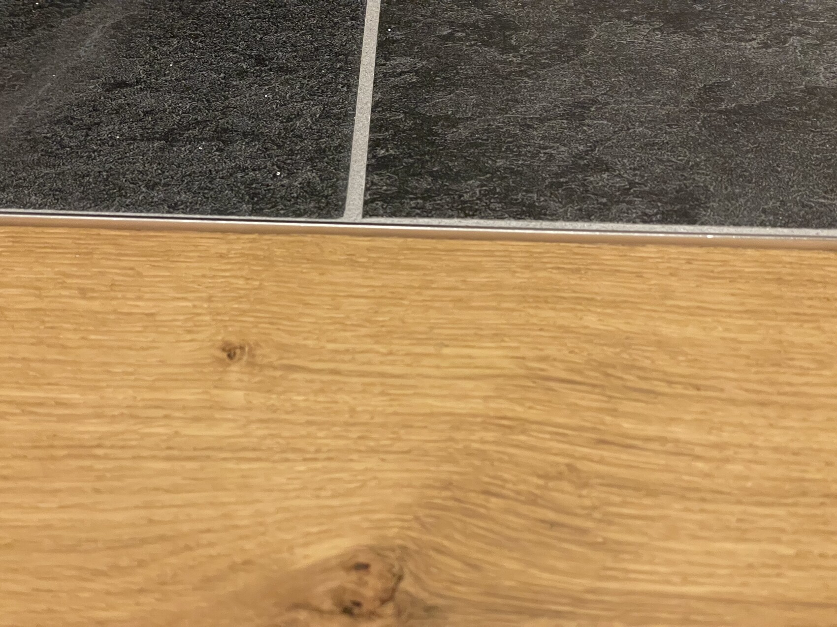 Übergang von dunklem Boden oben zu Holzboden unten, durch silberne Metallleiste getrennt.