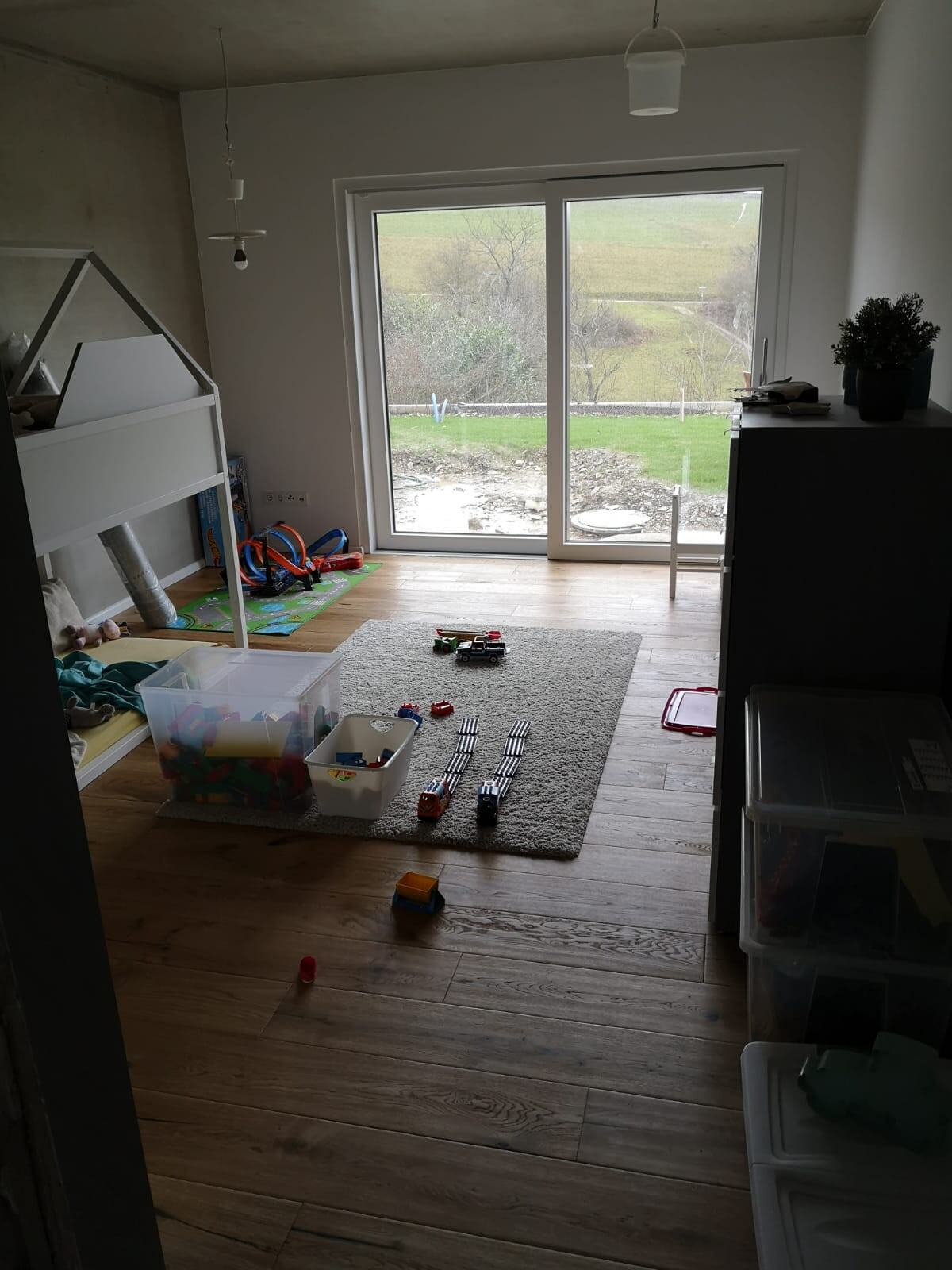Kleines Kinderzimmer mit Hochbett links, Spielteppich, Spielzeug und großes Fenster zum Garten