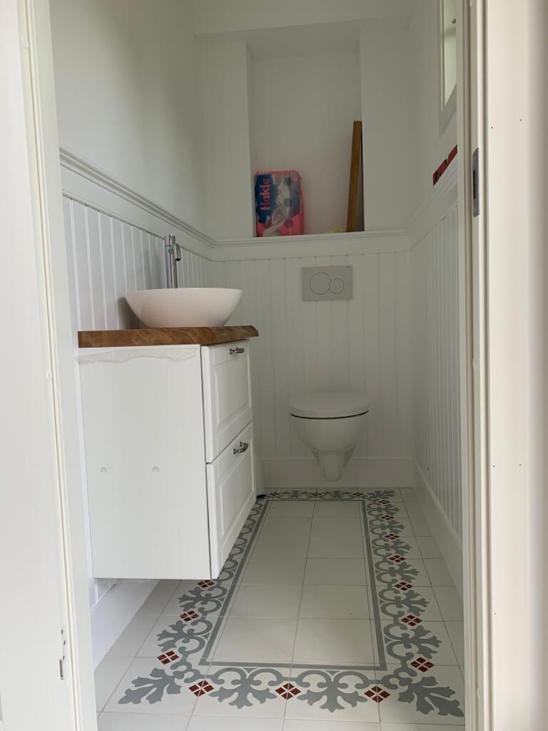 Kleines Bad: Wand-WC, Waschbecken auf Holzplatte, weißer Unterschrank, dekorativer Fliesenboden.