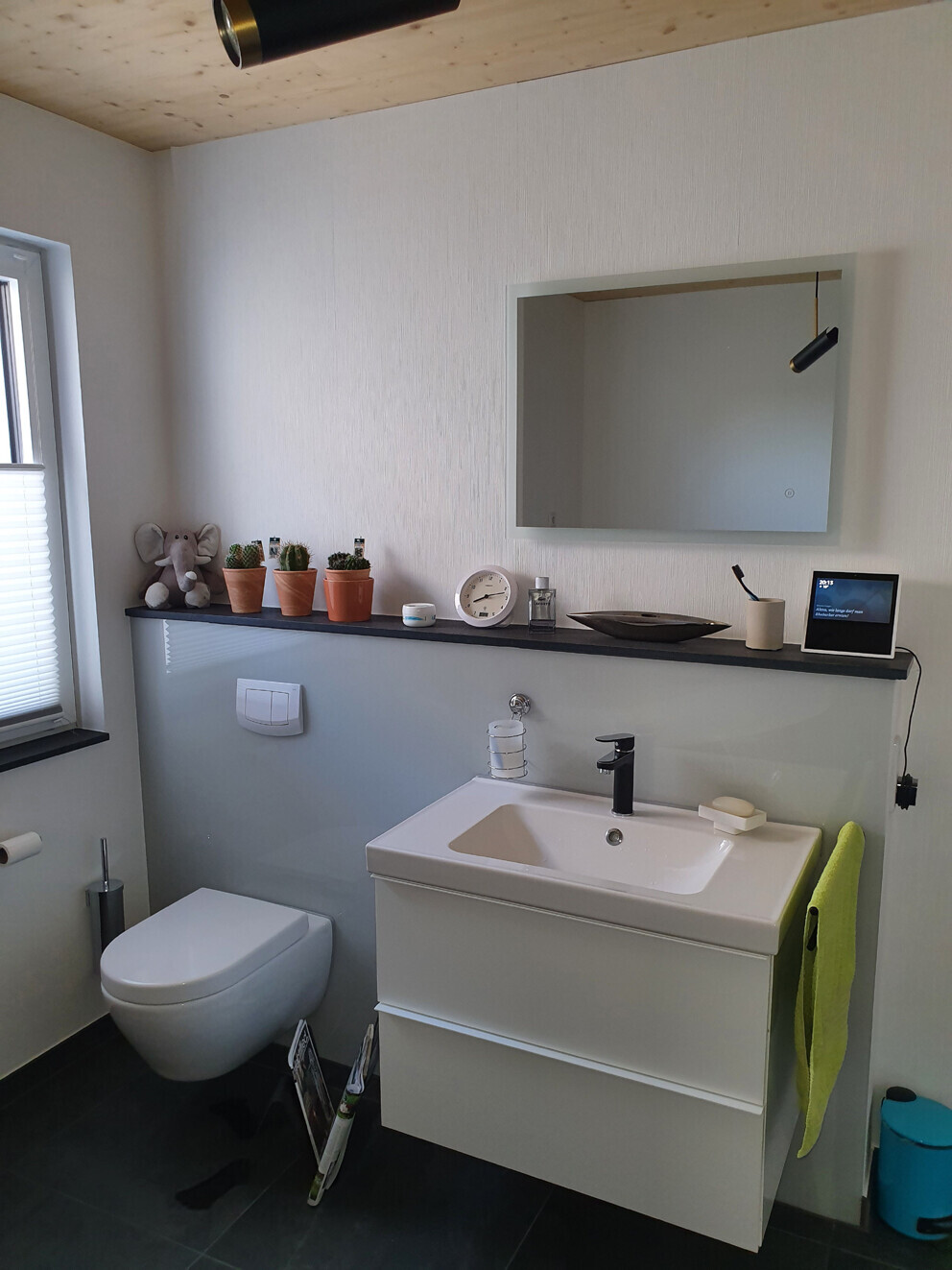 Modernes Bad mit Wand-WC, weißem Waschtisch, Spiegel, Pflanzenecke und grünem Handtuch