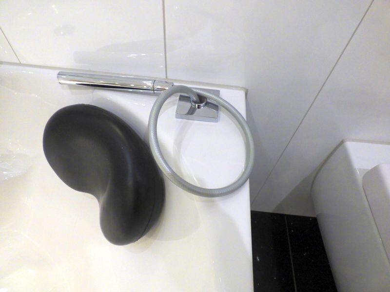 Schwarze Brustprothese liegt auf weißem Waschbecken, daneben runder Handtuchring an der Wand.