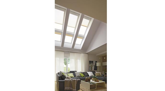 Helles Wohnzimmer mit großen Dachfenstern, grauer Sofakombo, Kissen und Couchtisch.