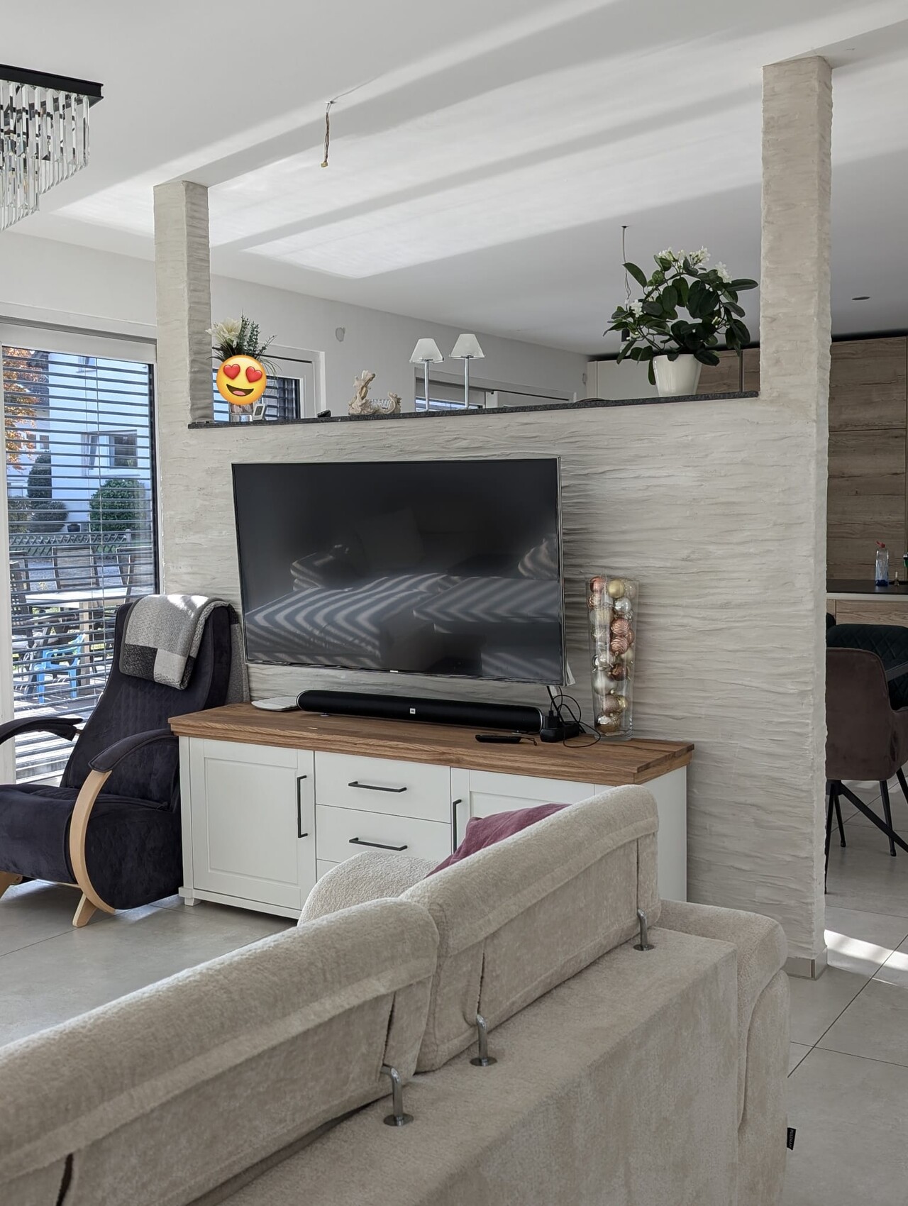 Wohnzimmer mit Flachbild-TV an der weißen Trennwand, Sofa, Couchtisch und Pflanzen.