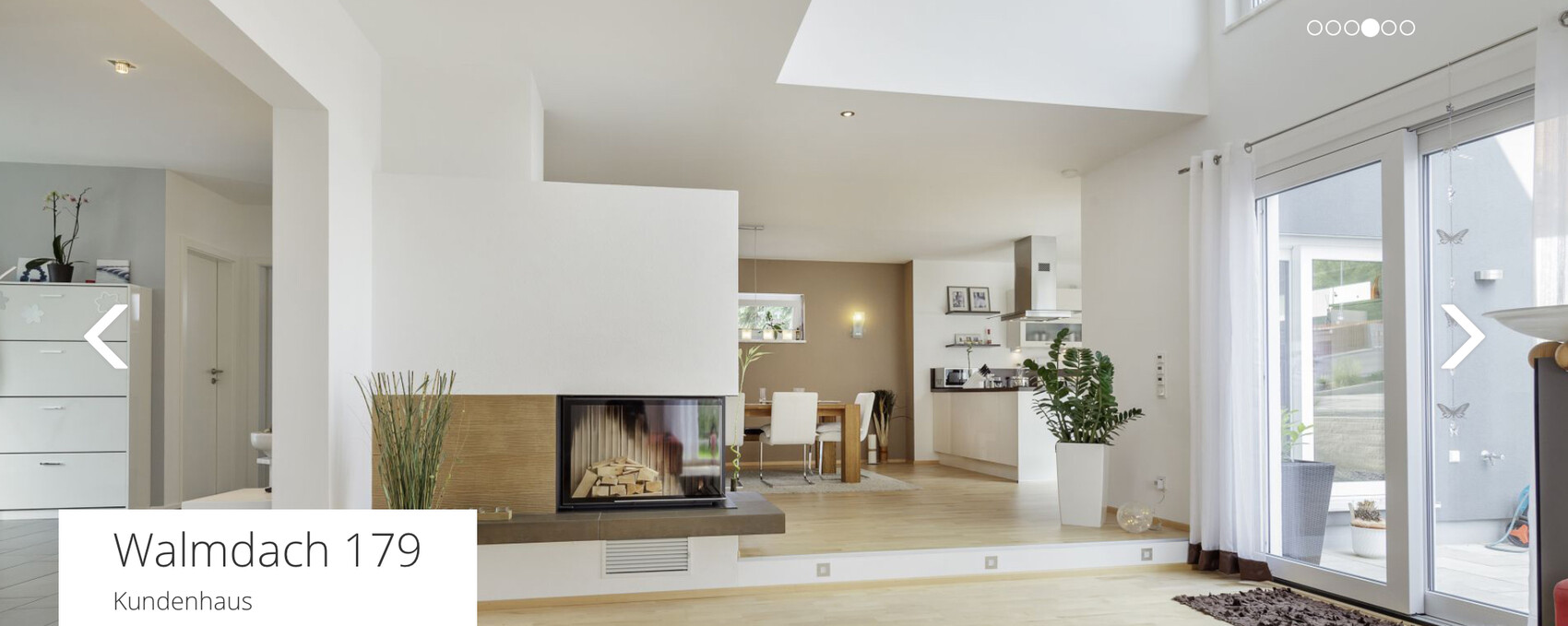 Offener Wohn- und Essbereich mit Kamin, moderner Küche, Holzboden und großen Glastüren.